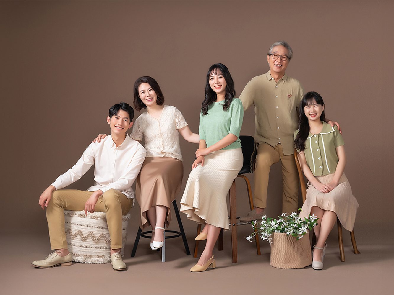 창원 캐주얼 가족사진 — 다섯 식구가 스툴과 의자에 앉아 서로에게 손을 얹었습니다. 베이지와 연두가 배경과 자연스럽게 이어집니다