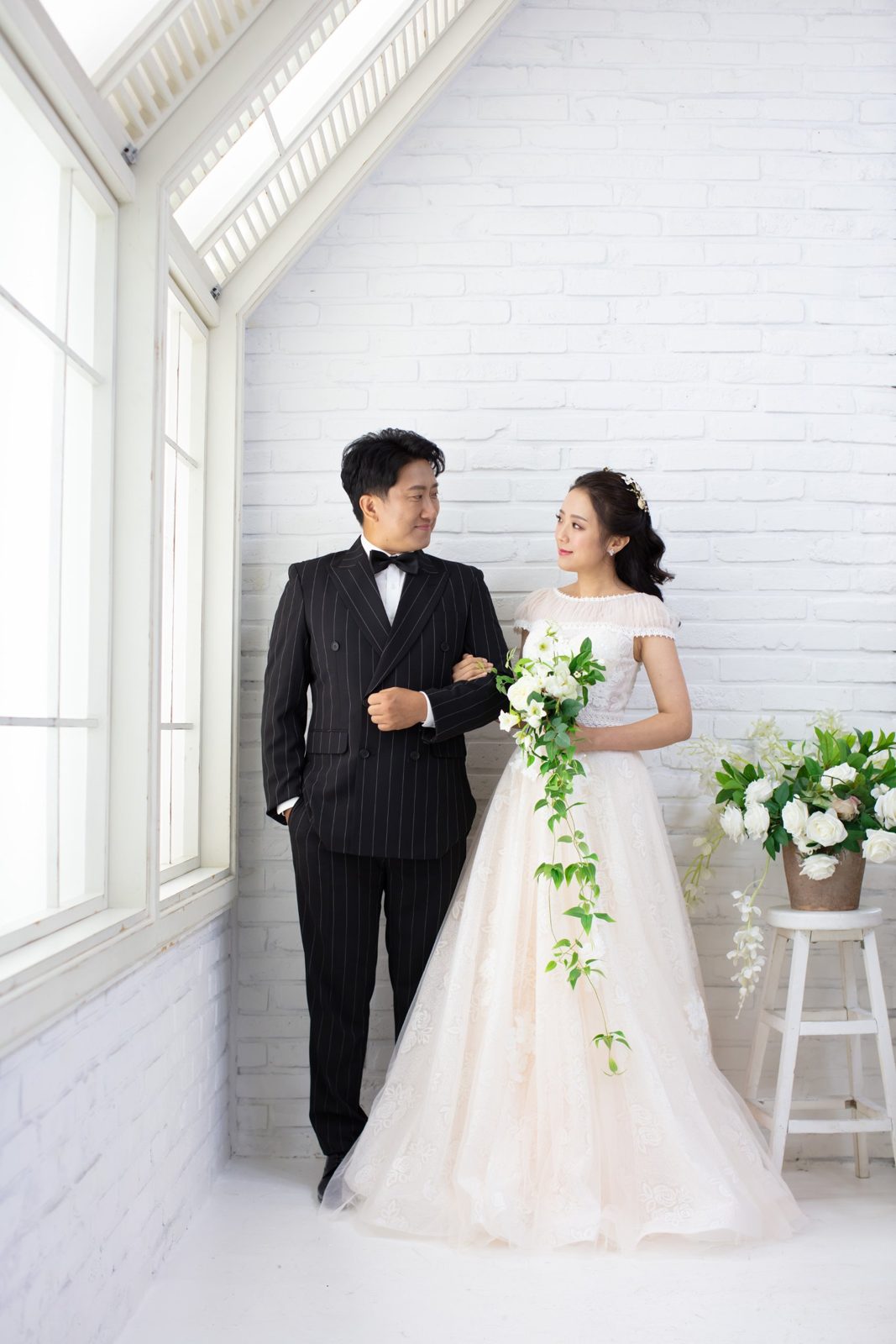 웨딩 컨셉 촬영 스타일 예시 이미지 — 창가에서 찍은 드레스와 정장