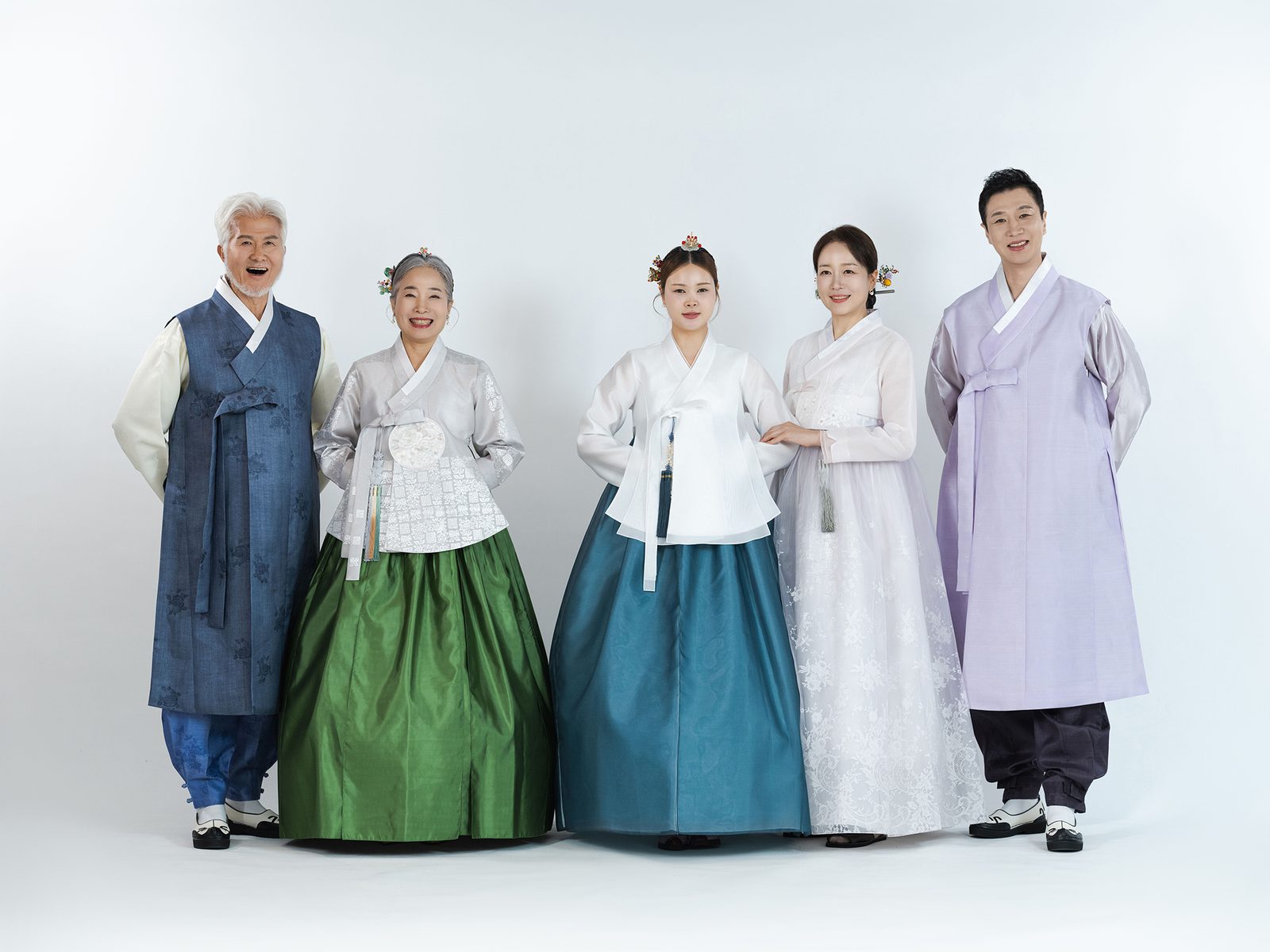 의령 한복 가족사진 — 흰 배경 앞에 선 다섯 사람. 할머니는 초록 치마, 두 젊은 여성은 청록과 흰색, 두 남성은 남색과 연보라 두루마기입니다