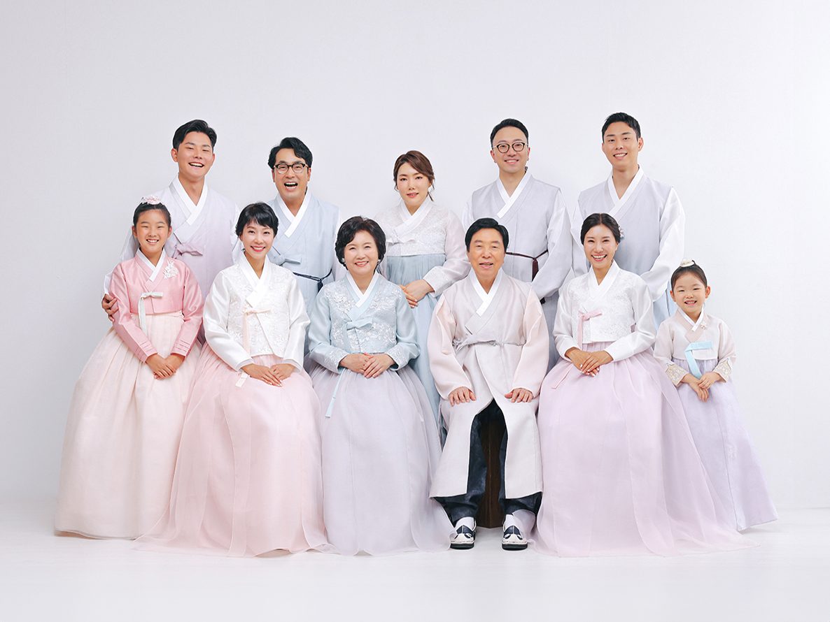 의령 한복 가족사진 — 흰 배경 앞 열한 사람. 분홍과 연보라, 연한 회색으로 세대가 고르게 섞였습니다