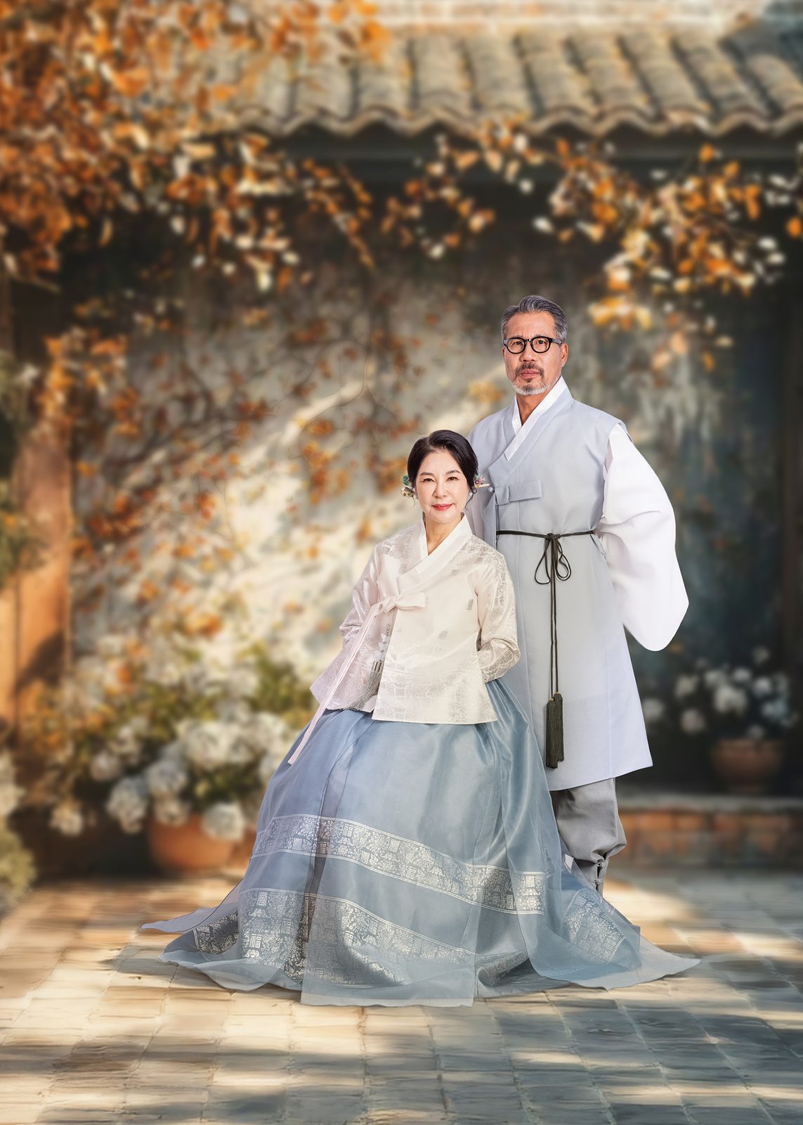 창원 한복 부부사진 — 가을 잎이 내려앉은 배경 앞. 어르신 부부가 아내는 무릎을 꿇고 남편은 뒤에 섰습니다