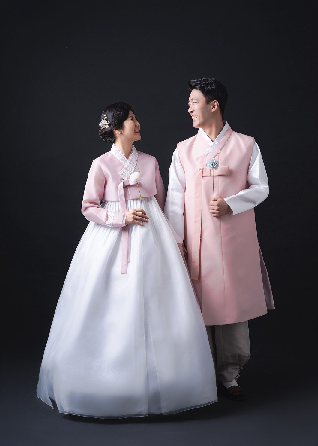창원 한복 부부사진 — 검정 배경 앞에서 마주 보는 두 사람. 분홍 저고리와 분홍 두루마기입니다