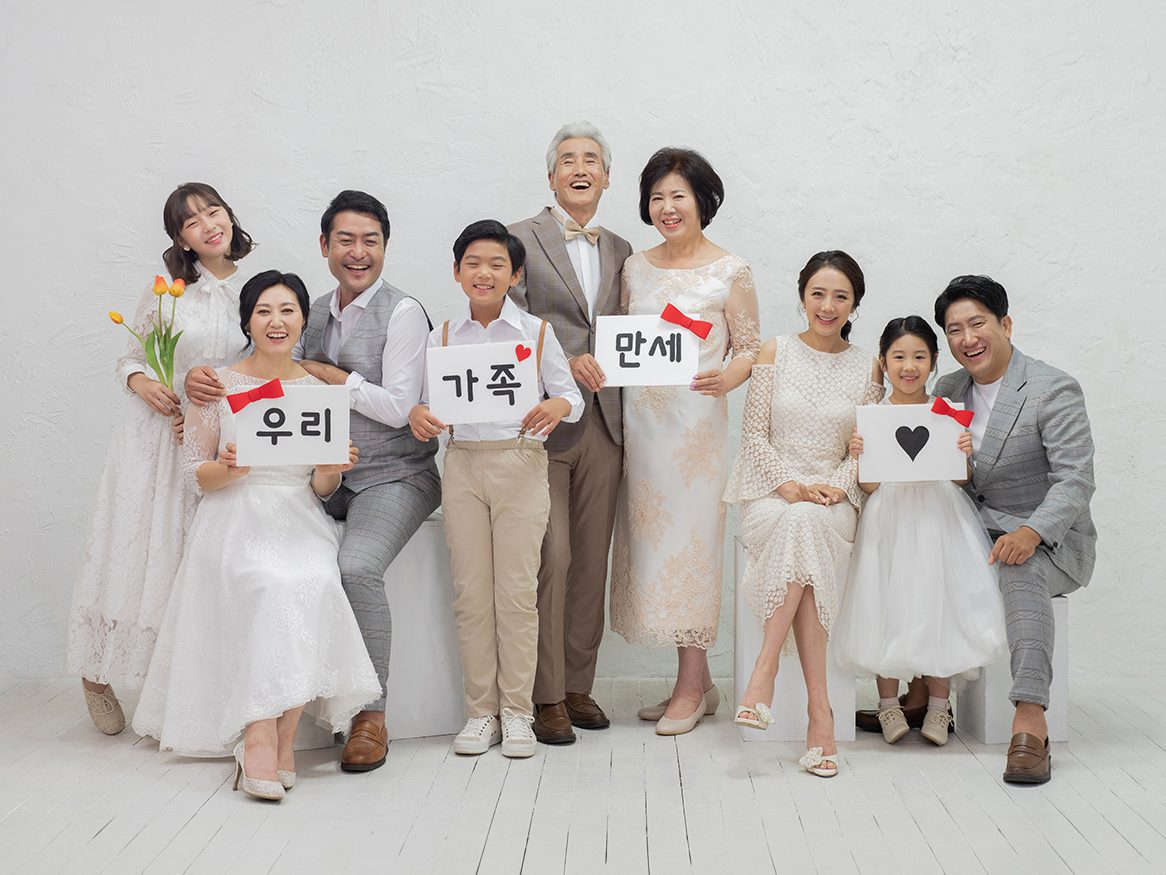 창원 세미웨딩 가족사진 — 팻말과 튤립을 든 여덟 사람. '우리', '가족', '만세' 글자가 사진의 표정을 만듭니다