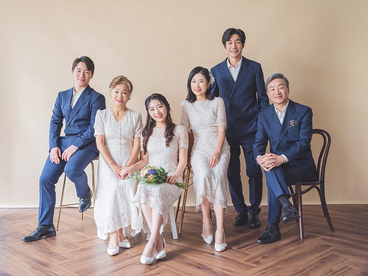 창원 세미웨딩 가족사진 — 네이비 수트와 흰 드레스, 여섯 사람. 헤링본 바닥이 사진의 아래쪽을 잡아 줍니다